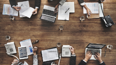 An overhead shot showing a group of people sitting around a table working. This picture demonstrates the power of alignment and howcollaboration is key to bring together workflows, policies, definitions, and rules.